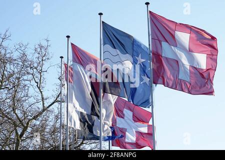 Schweizer Bundesflagge, kantonale Flagge des Kantons Aargau und kommunale Flagge der Stadt Baden. Sie winken im Wind auf Metallstangen im Hintergrund. Stockfoto