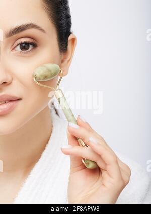 Face Jade Roller. Das halboffene Gesicht einer hispanischen Frau mit Jade oder Steinrolle für Anti-Aging-Verfahren Stockfoto