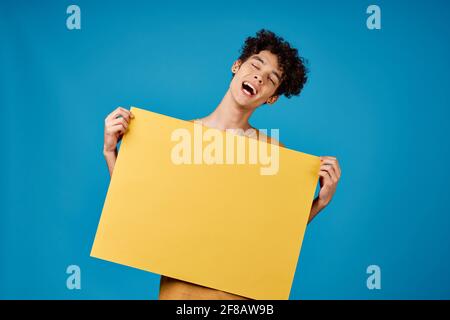 Lustige lockige Jungs mit einem gelb scharfen Werbung Copy Space Blauer Hintergrund Stockfoto