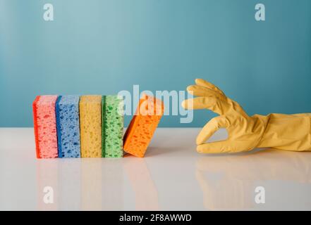 Handschuhen mit OK-Geste und bunten Putzschwämmen auf blauem Hintergrund. Reinigungsservice und Frühjahrsputz-Konzept Stockfoto