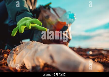 Ein Arbeiter in Gummischuhen sammelt Müll an einem Meeresstrand. Nahaufnahme der Hand. Das Konzept des Erdtages und das Problem der Ökologie. Ansicht von unten. Stockfoto