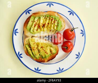 Avocado-Scheiben auf knusprigem weißem Toast mit roten Paprikaflocken und Kirschtomaten. Von oben in quadratischer Zusammensetzung. Stockfoto