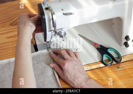 Frau mittleren Alters Hände nähen Leinentuch auf Nähmaschine, von oben Draufsicht, Handwerk, Slow Fashion, Alltagsmomente und eco Stockfoto