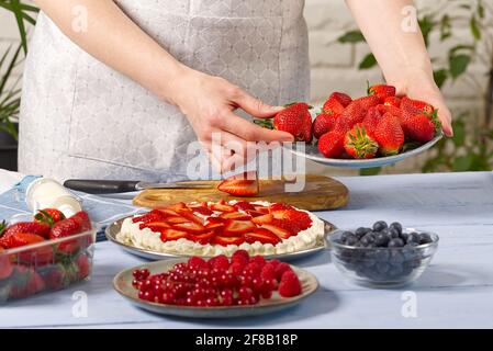 Die Bäckerin stapelt Erdbeeren auf der Basis des Bades aus Baiser-Erdbeerkuchen. Hausgemachter Erdbeerkuchen aus Baiser-Kuchen und Rahm mit Erdbeeren. Stockfoto