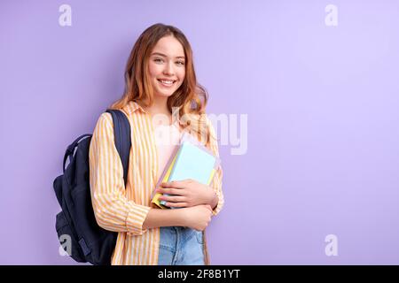 Diligent Schüchtern Kaukasischen Student Girl Trägt Schultasche Und Bücher Posieren Bei Der Kamera, Intelligente Weibliche Isoliert Auf Lila Violetten Hintergrund Stockfoto