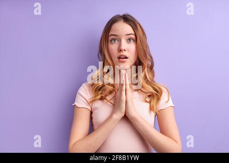 Attraktives blondes Mädchen in legerer Kleidung betet für das Wohlbefinden der Familie, hält die Handflächen in Gebetsgesten zusammengedrückt, träumt und schaut nach oben. Studi Stockfoto