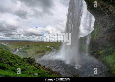 Blick von hinten auf den Seljalandsfoss Wasserfall in Island an einem kalten, bewölkten Frühlingstag. Stockfoto