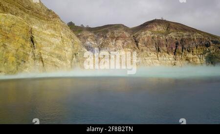 Flug über die Vulanice Seen in geringer Höhe. Nahaufnahme einer Felswand, die bunte Seen trennt. Der dreifarbige Krater des Kelimutu-Vulkans ist bedeckt Stockfoto