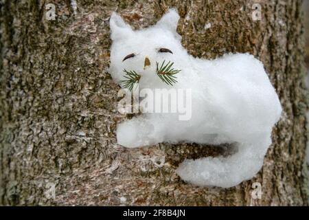 Kreativer Ansatz für Kinder. Die Kinder steckten eine Schneefigur einer Katze auf einen Baum (wie ein Hochrelief). Stockfoto