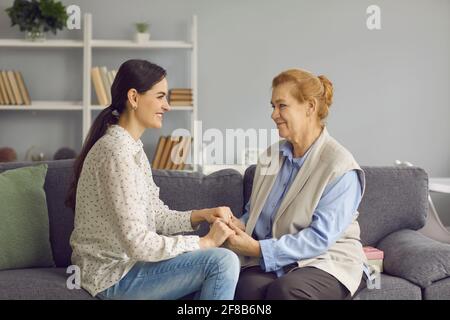 Lächelnde ältere Mutter und Erwachsene Tochter halten die Hände zusammen sitzen Auf dem Sofa Stockfoto