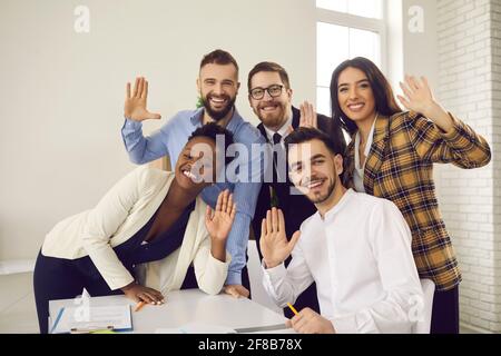 Gruppenportrait von glücklichen jungen Geschäftsleuten, die mit den Händen zuwinken Kamera und Lächeln Stockfoto