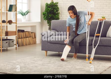 Frau mit gebrochenem Bein im Cast, die versucht aufzustehen Mit Krücken Stockfoto