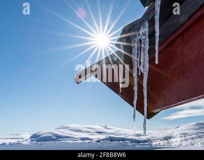 Nahaufnahme eines langen Eiszapfes, der an einem kalten Wintertag vom Dach hängt. Stockfoto