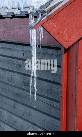 Nahaufnahme eines langen Eiszapfes, der an einem kalten Wintertag vom Dach hängt. Stockfoto