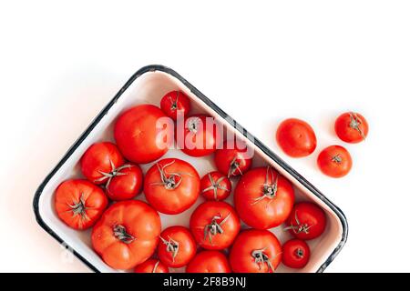 Reife Tomaten in verschiedenen Größen in einer Emaille-Schüssel auf dem Tisch, Draufsicht Stockfoto