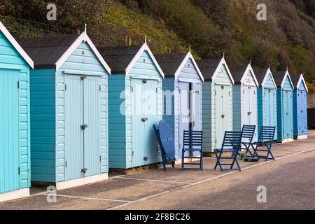 Paint it blue - Reihe von verschiedenen Schattierungen von blauen Strandhütten mit blauem Tisch und Stühlen draußen an der Promenade am Bournemouth Beach, Dorset UK im April Stockfoto