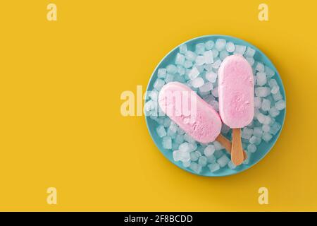 Erdbeerpopsicles und zerkleinertes Eis auf blauer Platte auf gelb Hintergrund Stockfoto