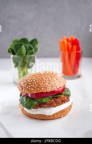 Veganer Burger mit roten Bohnen, rotem Pfeffer, Spinat, weißem Joghurt und frischen Salatblättern und geschnittenem Gemüse im Hintergrund. Stockfoto