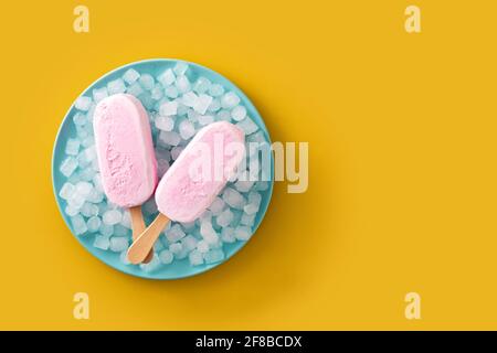 Erdbeerpopsicles und zerkleinertes Eis auf blauer Platte auf gelb Hintergrund Stockfoto