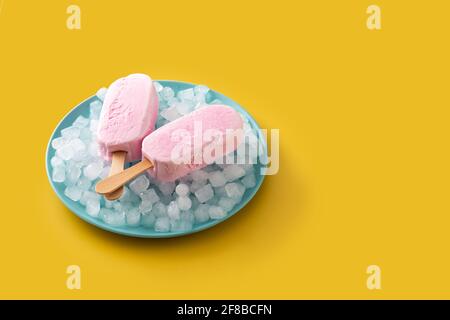 Erdbeerpopsicles und zerkleinertes Eis auf blauer Platte auf gelb Hintergrund Stockfoto
