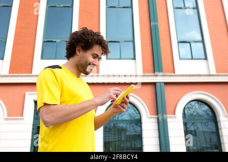 Der junge Latino-Athlet im gelben T-Shirt sieht ihn an Handy nach dem Training Stockfoto