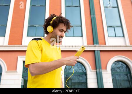 Junger lateinischer Athlet in gelbem T-Shirt bereitet sich darauf vor Hören Sie bei einer Trainingseinheit Musik mit Kopfhörern Stockfoto