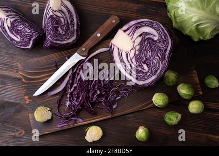 Gehackter Rotkohl auf einem Schneidebrett auf einem dunklen Holzhintergrund mit frühem Kohlkopf, rosenkohl, rustikaler Stil, Nahaufnahme. Stockfoto