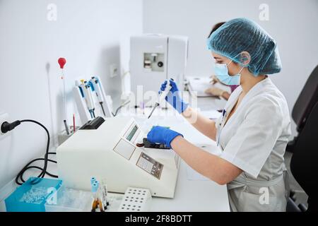 Wissenschaftler mit Latexhandschuhen, die an einem halbautomatischen Biochemie-Analysator arbeiten Stockfoto