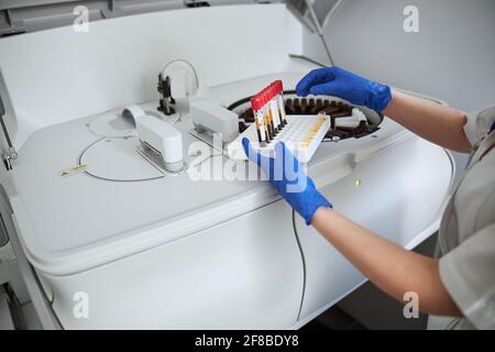 Frau Biochemikerin, die mit Blutproben an einem chemischen Analysator steht Stockfoto