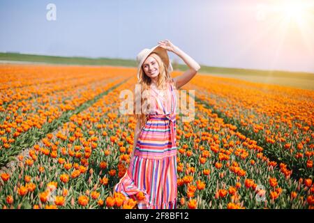 Schöne Frau mit roten Haaren in gestreiftem Kleid, die auf bunten Tulpenfeldern in Amsterdam, Holland, steht. Zauberhafte holländische Landschaft mit Tulpenfeld. Trevel- und Federkonzept. Stockfoto