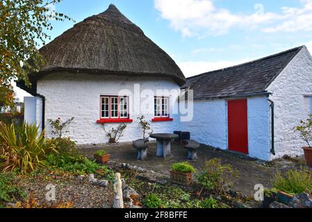 Ursprüngliches Haus aus dem 19. Jahrhundert mit Strohdach und weiß gestrichenen Wänden, roten Holzfenstern und Steinmöbeln auf der Veranda in Adare, Limerick, Irland. Stockfoto