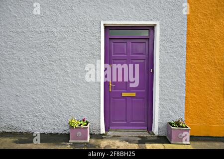 Ländliche Hausfassade mit einer weißen strukturierten Wand und einer lila Tür mit einem Bronzestiel und Briefkasten in Adare, Limerick Irland. Stockfoto