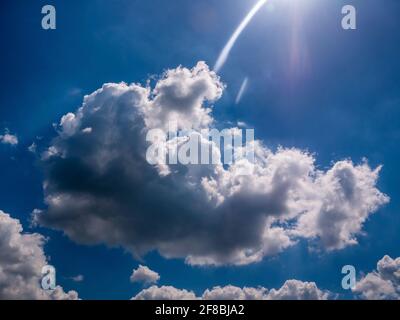 Wunderschöne flauschige Wolke am blauen Himmel, mit abgerundetem Sonnenstrahl Stockfoto