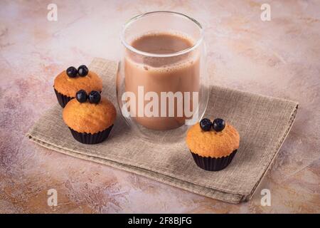 Ein Glas Kaffee und Muffins mit schwarzen Beeren. Cupcakes mit Johannisbeere und Heißgetränk auf dem Tisch, rustikales Stillleben. Braune Farben. Nachtisch Stockfoto