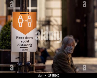 Kaukasischer Kaukasier, der ein Gesicht trägt und an einem sozialen Distanzierungsschild in York sitzt, nachdem er die Lockerung der Covid-19-Sperrbeschränkungen aufgehoben hatte. Stockfoto