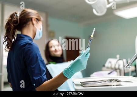 Junge Frau sitzt auf dem Zahnarztstuhl und der Zahnarzt untersucht sorgfältig die Zähne des Patienten. Der Zahnarzt konsultiert einen Patienten, der auf einem Stuhl sitzt Stockfoto