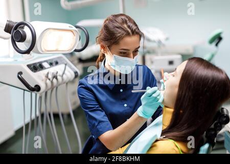 Junge Frau sitzt auf dem Zahnarztstuhl und der Zahnarzt untersucht sorgfältig die Zähne des Patienten. Der Zahnarzt konsultiert einen Patienten, der auf einem Stuhl sitzt Stockfoto