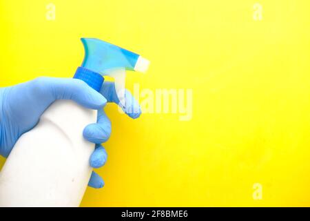 Hand in blauen Gummihandschuhen halten Sprühflasche auf gelb Hintergrund Stockfoto