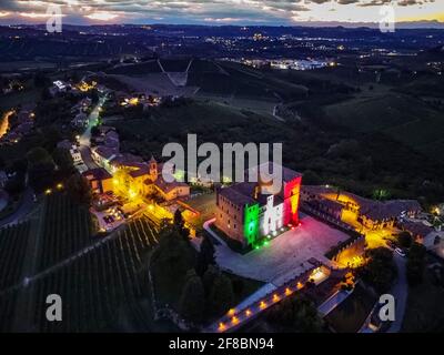 Nachtansicht der Stadt mit dem Schloss von Grinzane Cavour beleuchtet mit der italienischen Flagge in den Hügeln eingetaucht Mit den Weinbergen Stockfoto