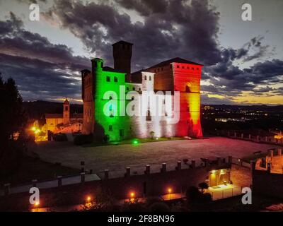 Nachtansicht des Schlosses von Grinzane Cavour beleuchtet mit Die italienische Flagge vor suggestiven Wolken Stockfoto