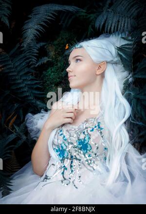 Foto eines ätherischen geheimnisvollen Elf-Mädchens mit silbernen langen Haare tragen schöne weiße Kleid mit Schmetterlingen und Silber Tiara In Farnen liegend Stockfoto