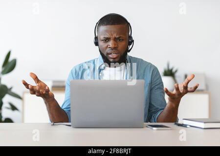 Arbeitsbelastung. Verärgerter Schwarzer Mann Im Headset Beim Blick Auf Den Laptop-Bildschirm Stockfoto