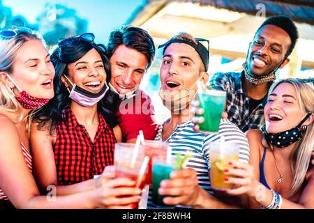 Fröhliche, multikulturelle Menschen, die in der Nachtbar mit offenem Gesicht toasten Masken - Neue normale Lebensstil Konzept mit milenial Freunde Gemeinsam Spaß haben Stockfoto