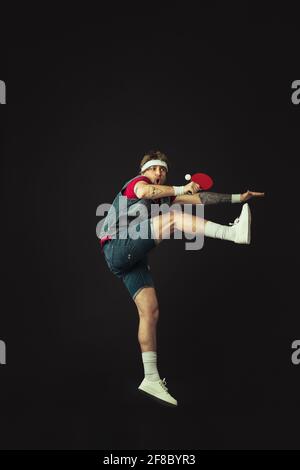 Junger kaukasischer lustiger Mann spielt Tischtennis isoliert auf schwarzem Hintergrund. Stockfoto