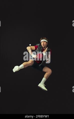 Junger kaukasischer lustiger Mann spielt Tischtennis isoliert auf schwarzem Hintergrund. Stockfoto