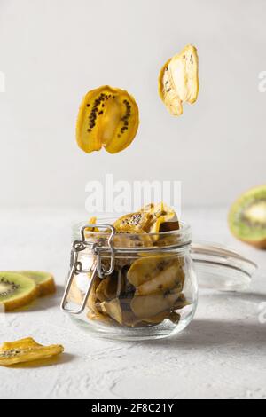 Kiwi-Chips glying to gell Glas für die Lagerung und Essen auf hellem Hintergrund, Heimtrocknung. Vegane, zuckerfreie Lebensmittel. Nahaufnahme. Vertikales Format. Stockfoto