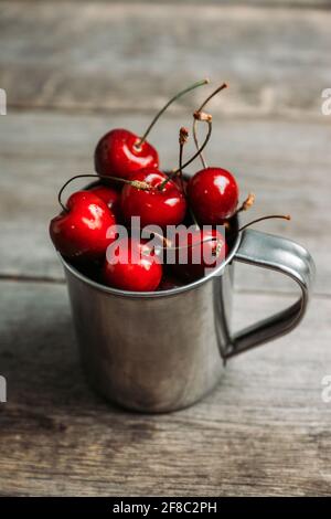 Reife und saftige Kirschen im alten Metallbecher auf dem dunklen rustikalen Hintergrund. Selektiver Fokus. Geringe Schärfentiefe. Stockfoto