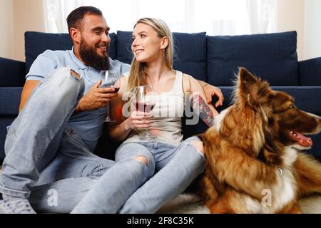 Nahaufnahme eines Pärchens, das mit ihrem Wein auf dem Sofa trinkt Border Collie Hund in der Nähe Stockfoto