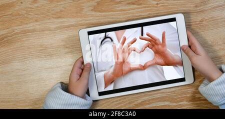 Geste Herz aus gefalteten Händen, eine Botschaft der Liebe und Fürsorge vom Arzt an den Patienten, durch den Bildschirm des Gadgets, in den Händen einer Frottee-Robe. Telemedizin. Stockfoto