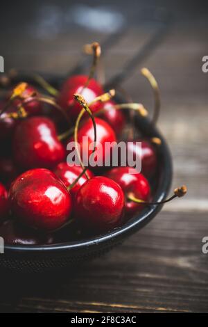 Reife und saftige Kirschen im schwarzen Metallsieb auf dem dunklen rustikalen Hintergrund. Selektiver Fokus. Geringe Schärfentiefe. Stockfoto